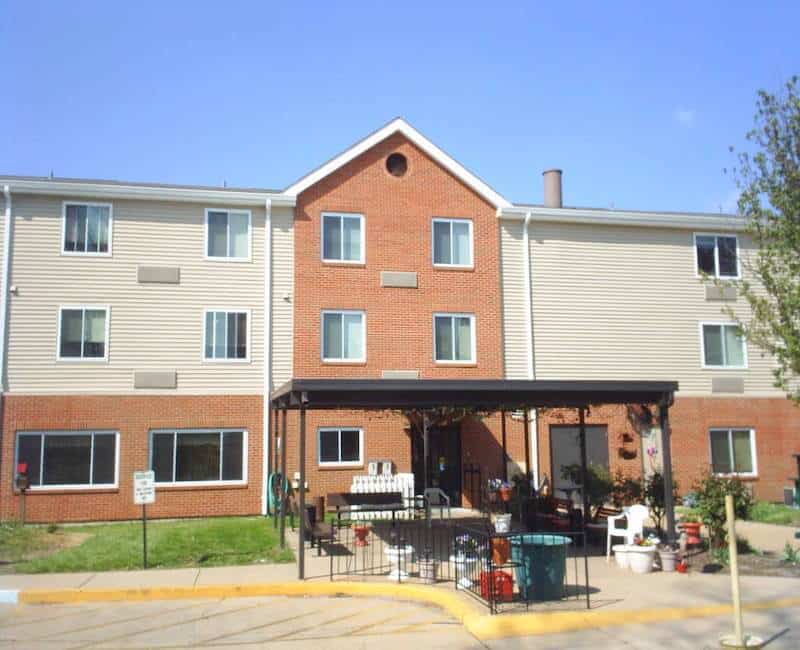 A three-story residential building with a brick facade and an entrance covered by an awning on a clear day.
