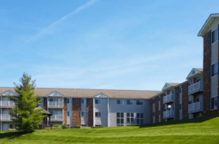 A residential apartment building with a well-maintained lawn under a clear blue sky.