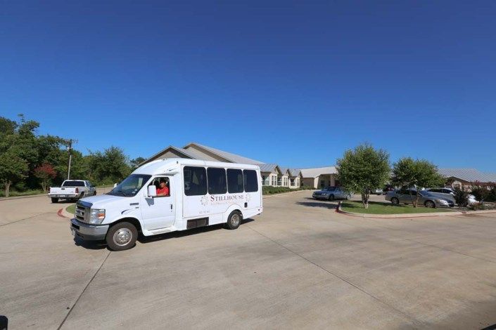A white van parked on a driveway near buildings under a clear blue sky.