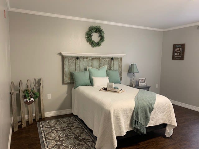 A cozy bedroom with a single bed featuring neutral-colored bedding and green accents, decorated with a wall wreath above the headboard.