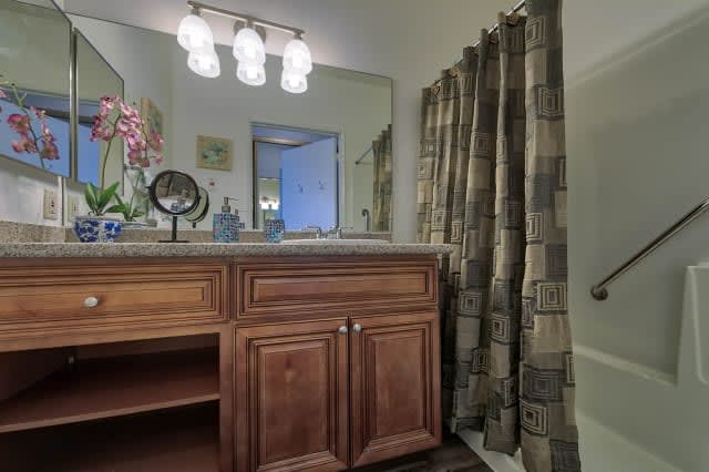 A modern bathroom with a wooden vanity, mirror, and a patterned shower curtain.