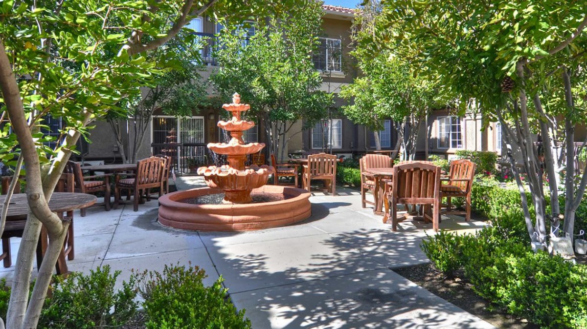 A tranquil courtyard featuring a central fountain surrounded by wooden outdoor seating and lush greenery.