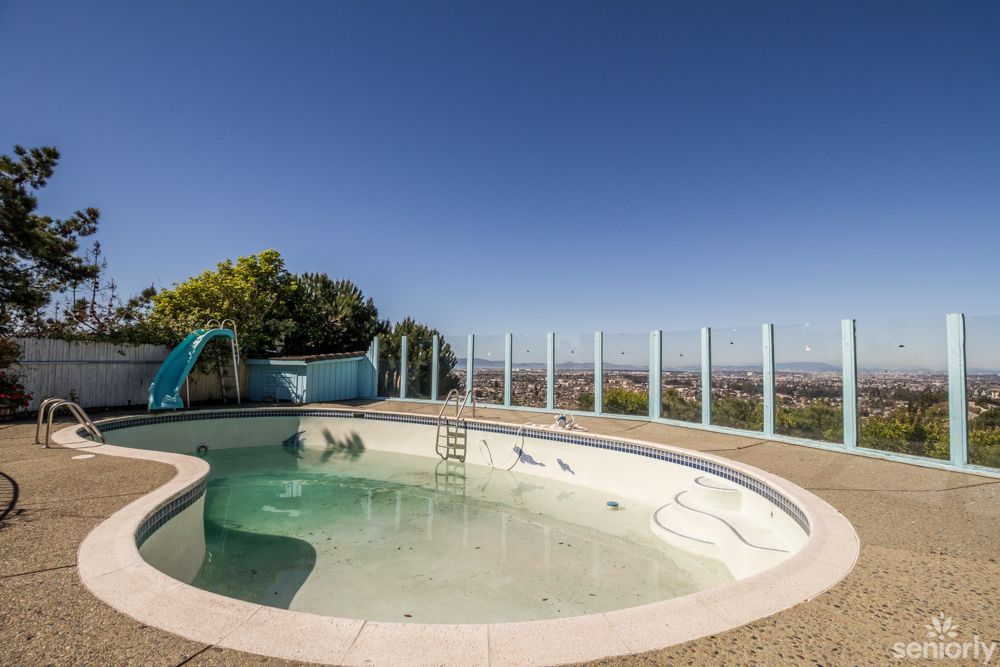 An outdoor circular pool with a slide, surrounded by a glass fence under a clear blue sky.