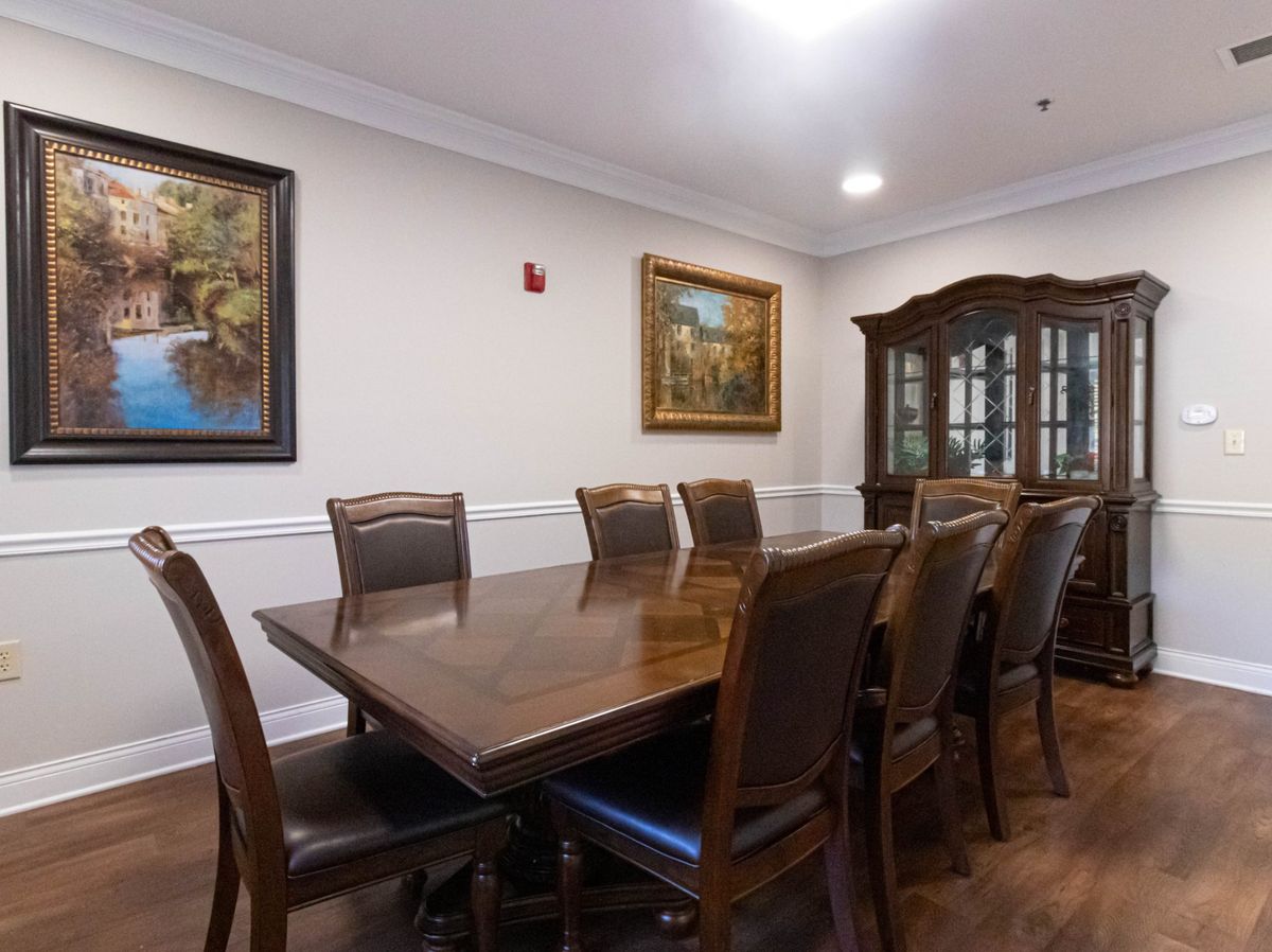 A spacious dining room with a long wooden table, surrounded by chairs and decorated with framed artwork on the walls.