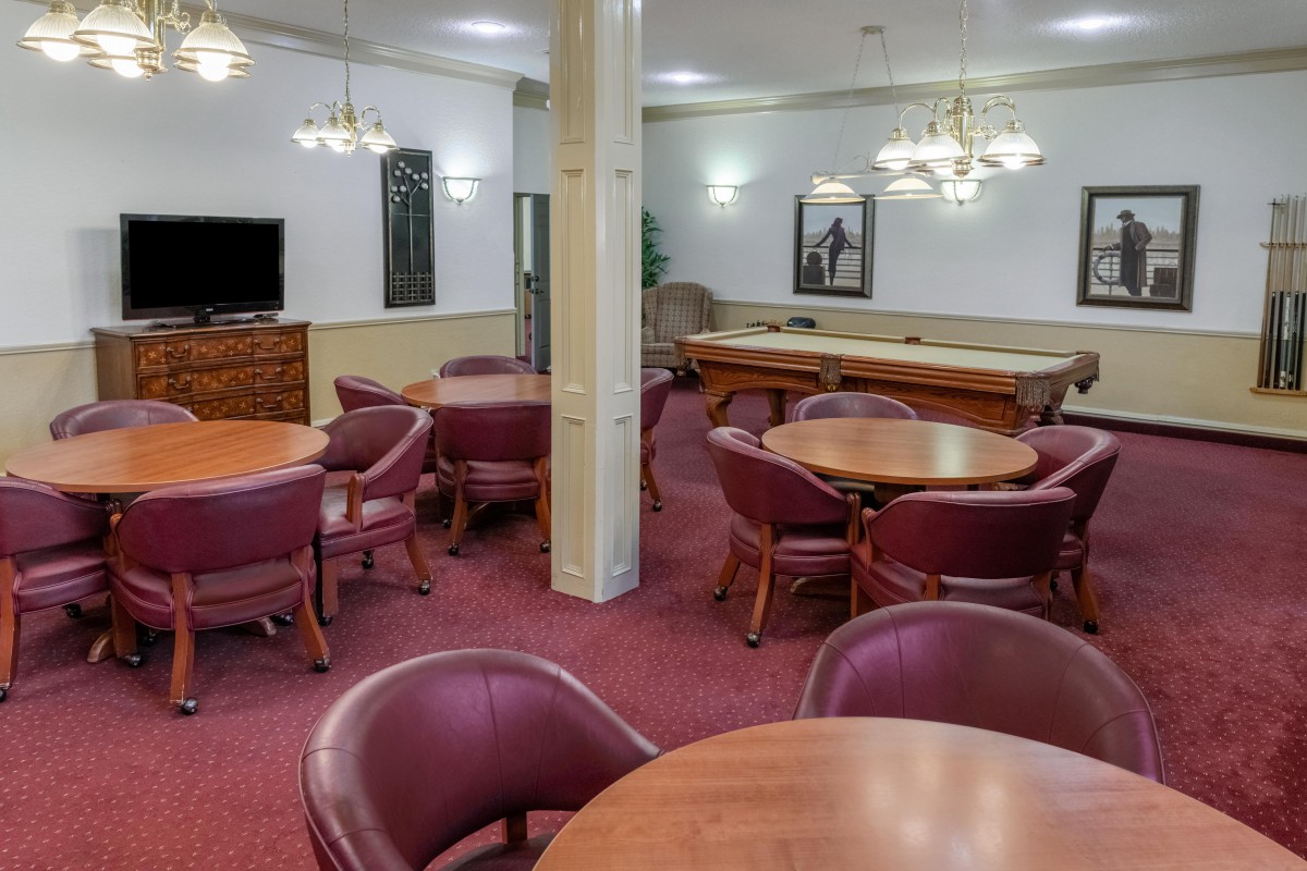 A spacious lounge area featuring multiple round tables with chairs, a pool table, and elegant lighting.