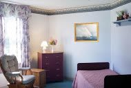 A cozy bedroom with a purple dresser, a table lamp, and wall art.