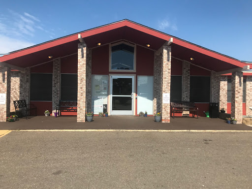 A modern building with a striking red roof and spacious entrance, surrounded by outdoor seating.