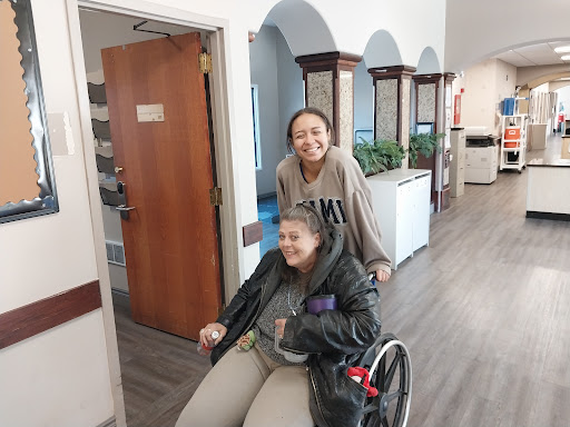 A joyful moment as one woman helps another in a wheelchair, showcasing friendship and support.