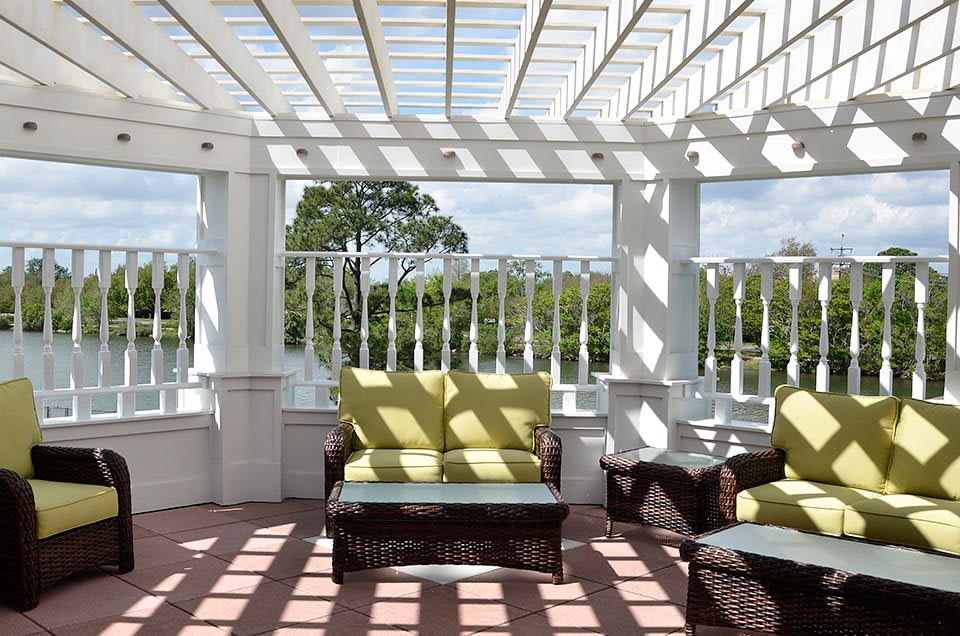 A sunlit patio with comfortable seating under a pergola, offering a scenic view.