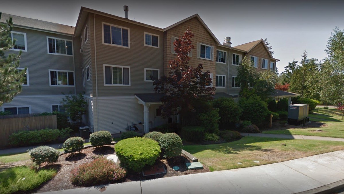 A residential building with a neatly landscaped front yard featuring bushes and a lawn.