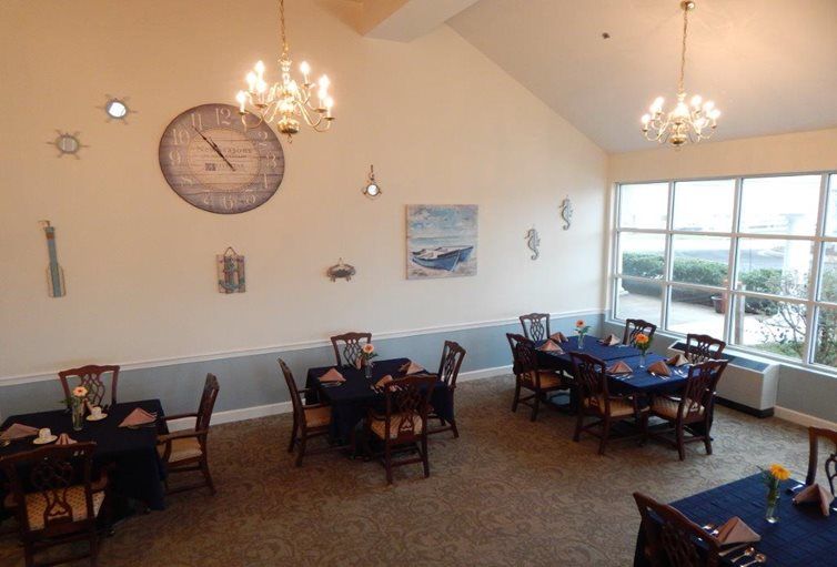 A cozy dining area with several tables and chairs, featuring a large wall clock and chandeliers.