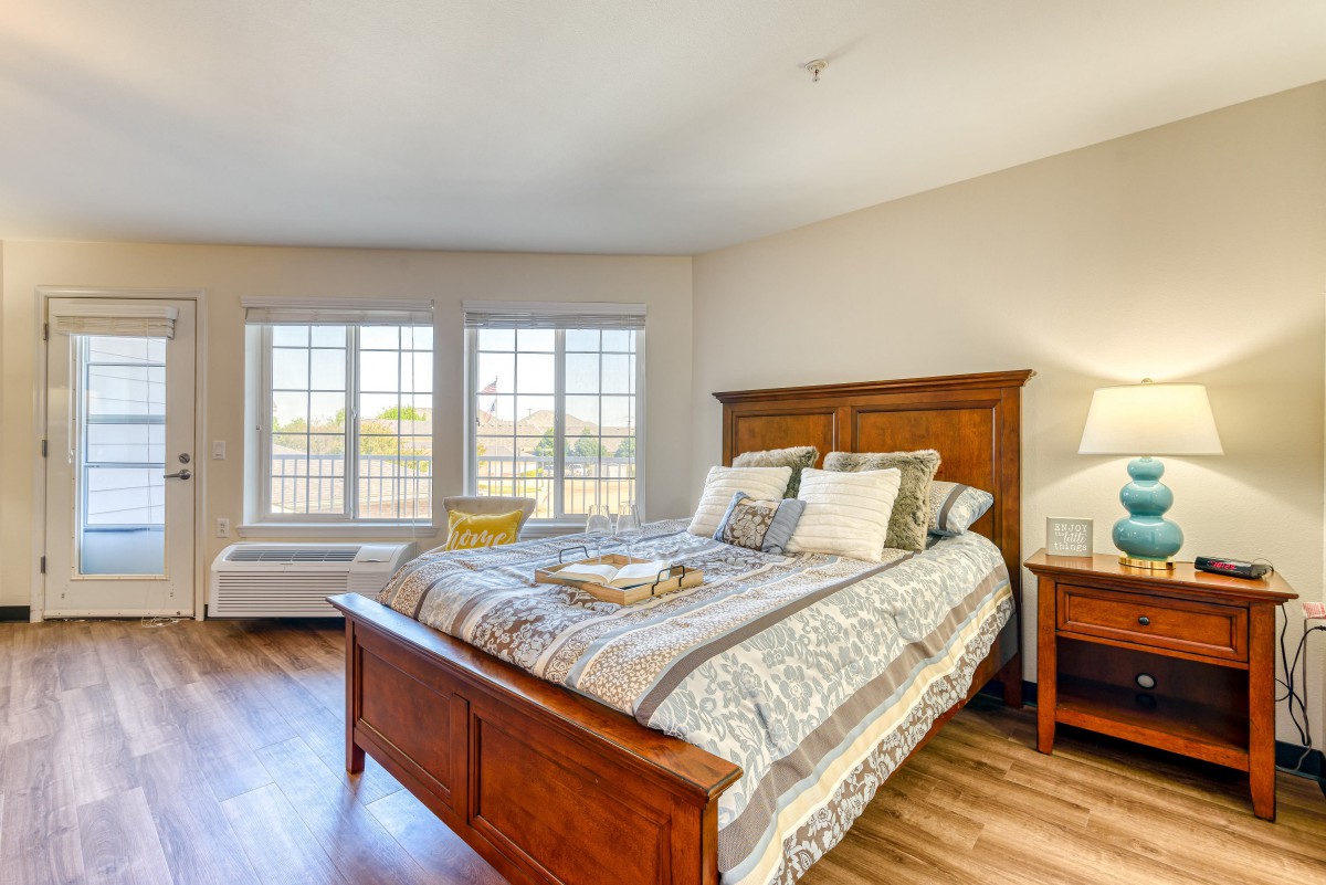 A cozy bedroom with a large wooden bed, soft lighting, and a view through the windows.
