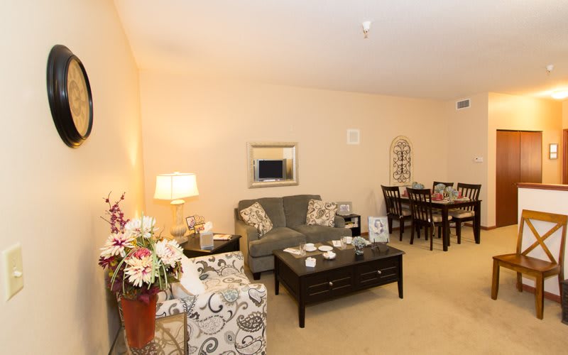 A warmly lit living room with a comfortable sofa, armchair, coffee table, and dining area.