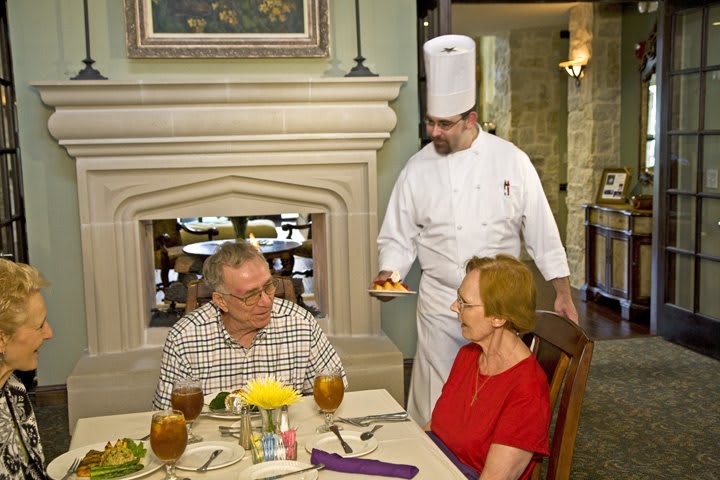 A chef presents a dish to a couple dining in a restaurant.