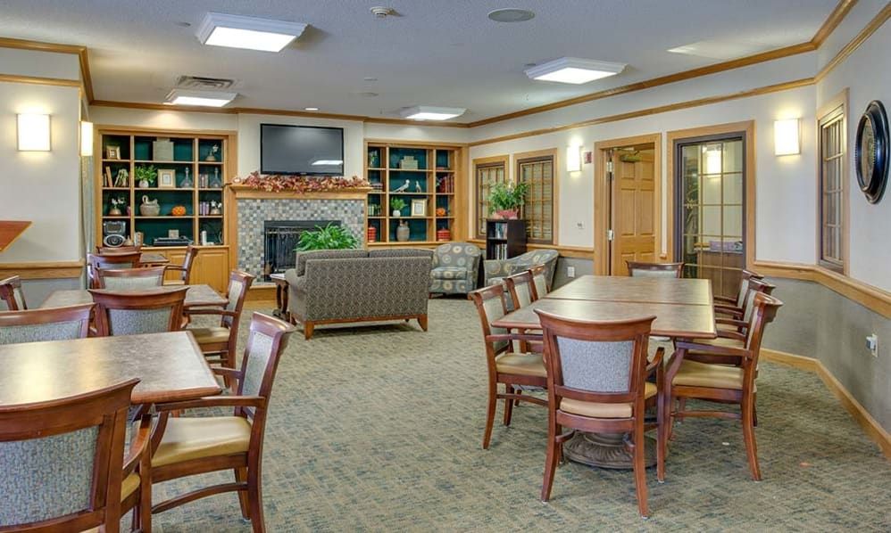 A cozy lounge area featuring tables, chairs, bookshelves, a television, and a fireplace.