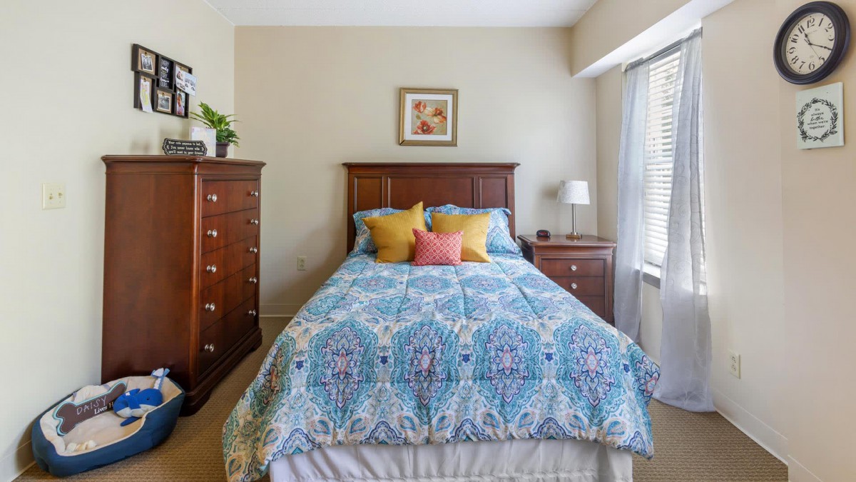 A cozy bedroom with a stylish bedspread and colorful pillows, featuring wooden furniture and natural light.
