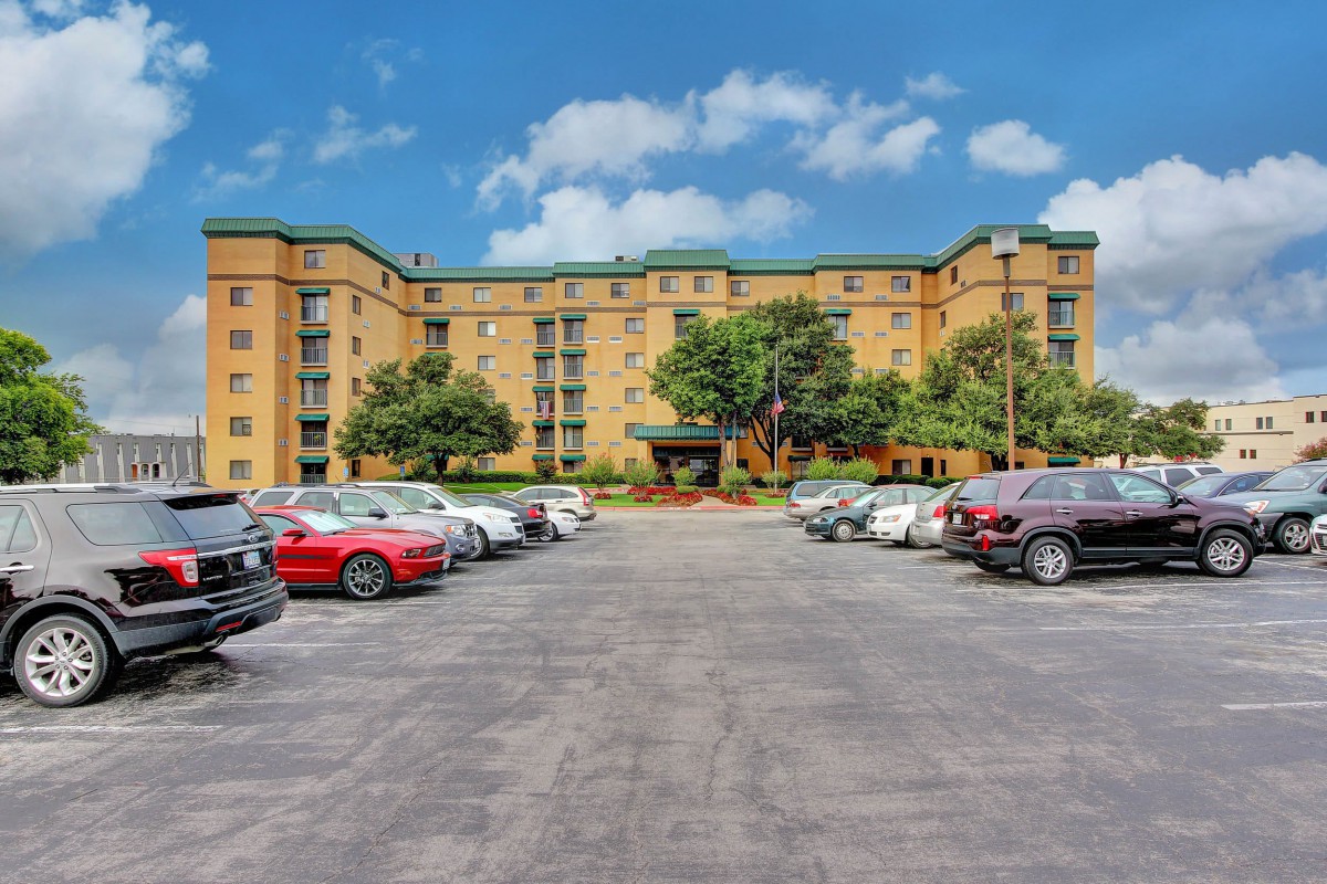 An apartment building with a parking lot filled with cars under a clear blue sky.