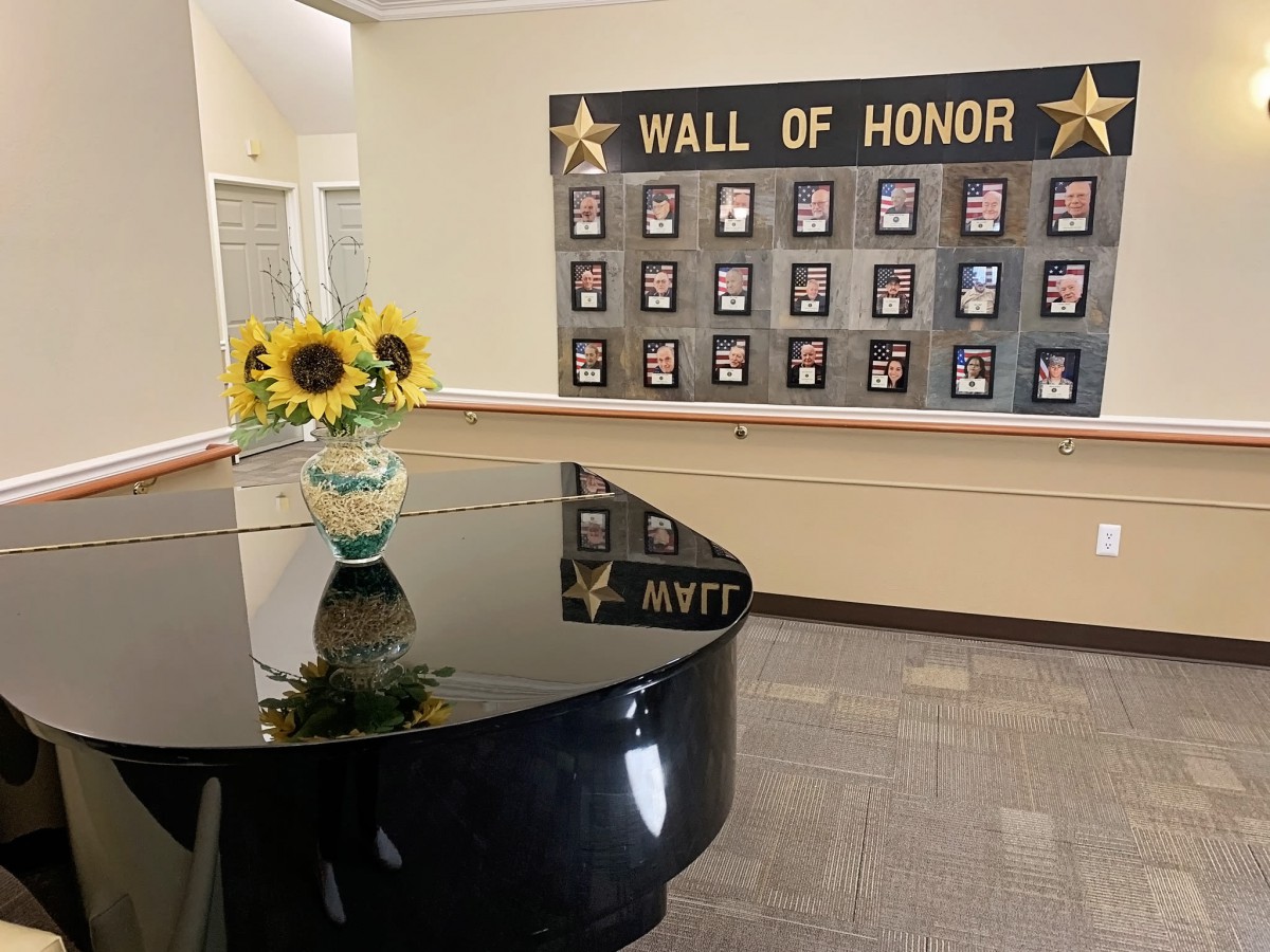 A Wall of Honor display featuring photographs, with a grand piano and sunflowers in the foreground.
