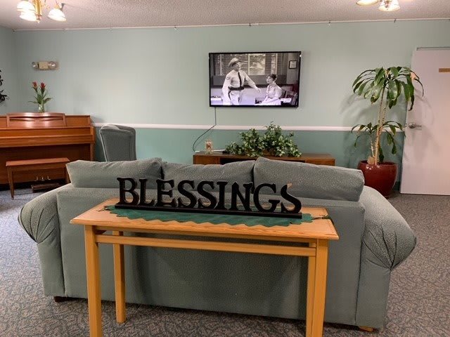 A cozy living room with a sofa, television, and decorative 'Blessings' sign.