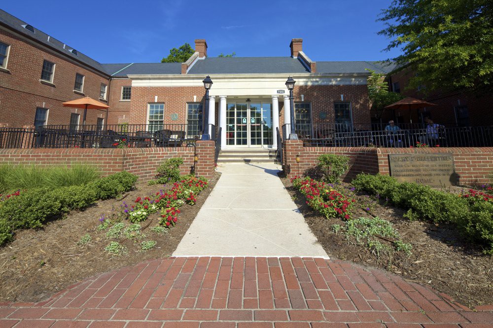 A brick building with a pathway leading to its entrance, surrounded by landscaped gardens.