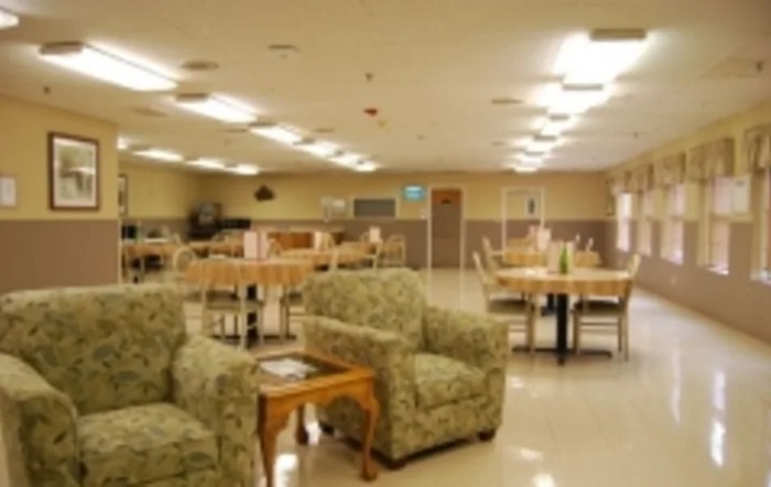 A spacious community room with armchairs and tables, featuring bright overhead lighting.
