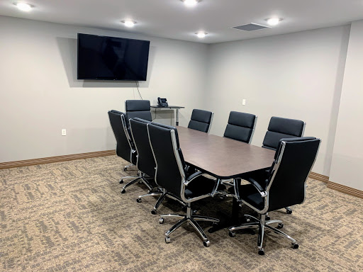 A modern meeting room equipped with a conference table, comfortable black chairs, and a wall-mounted television.