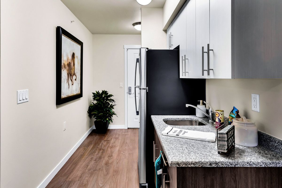A modern kitchen with granite countertops, white cabinets, and wooden flooring, featuring a piece of wall art and stainless steel appliances.