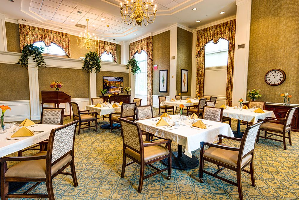 An elegantly decorated dining room with multiple tables and chairs, featuring a chandelier and tasteful decor.