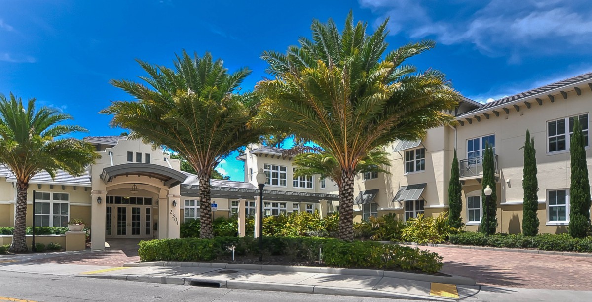 A sunny day view of a residential building with palm trees in front.