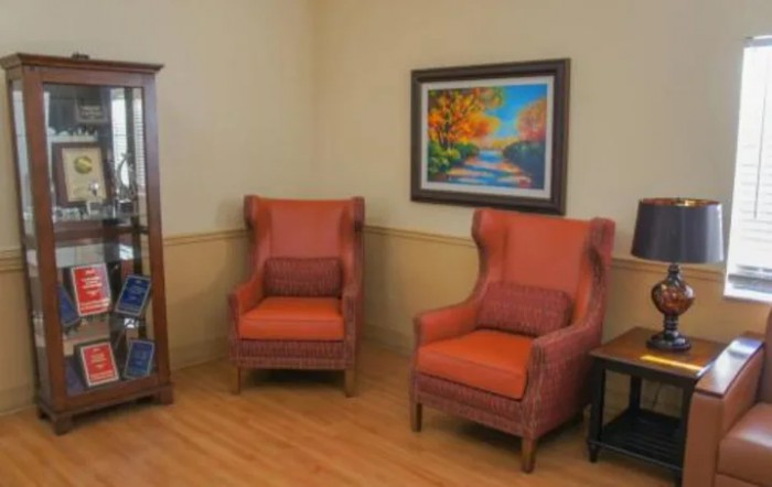 A cozy living room corner with two upholstered chairs, a colorful painting, and a bookshelf.