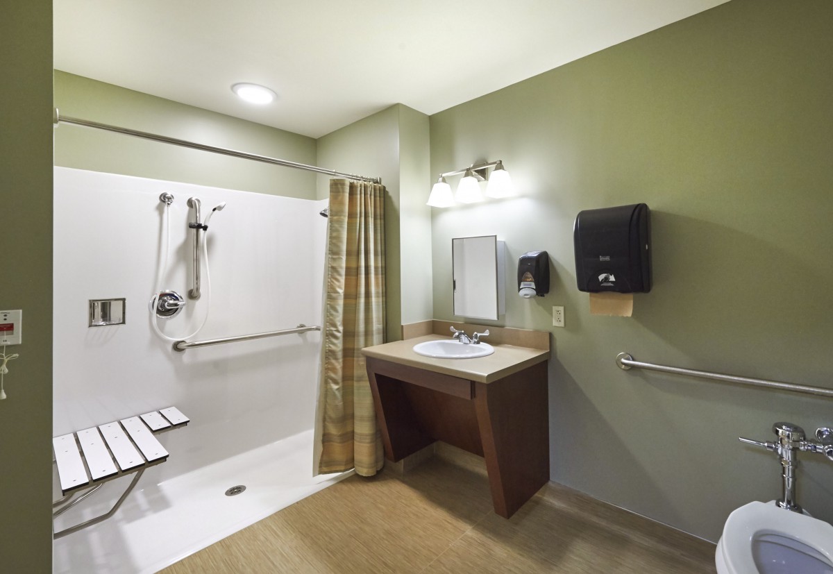 A modern, accessible bathroom featuring a walk-in shower with grab bars and a sink with ample counter space.