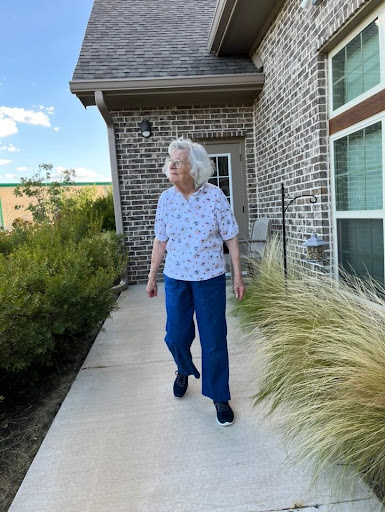 An elderly woman enjoying a stroll in her garden on a sunny day.