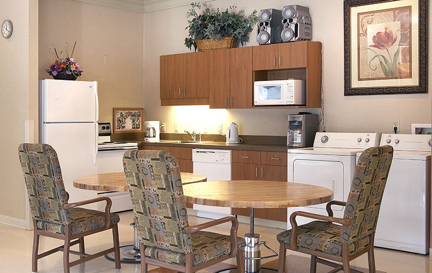 A modern kitchen with wooden cabinets, a table with chairs, and various appliances including a refrigerator and microwave.