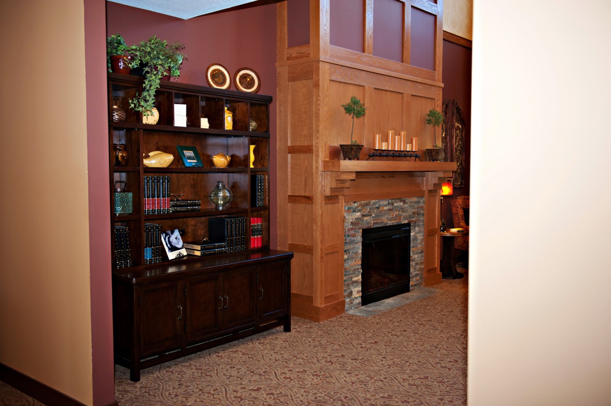 A cozy living room featuring a stone-faced fireplace and a dark wood bookshelf filled with books and decorative items.