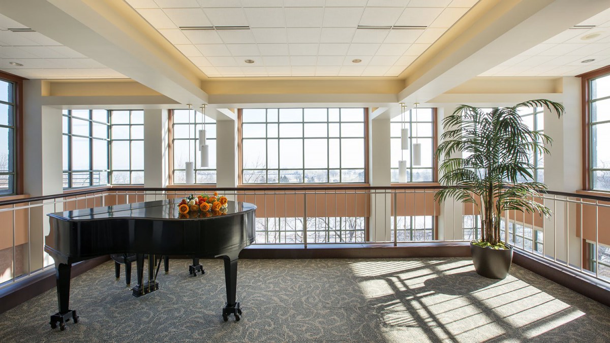 A grand piano sits in a sunlit room with large windows and a view.
