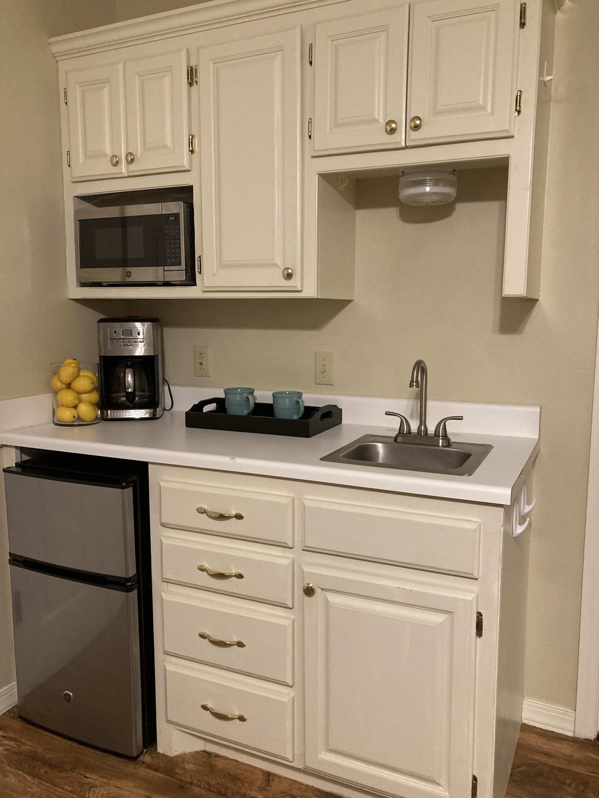 A compact kitchen area with a microwave, coffee maker, sink, and mini fridge.