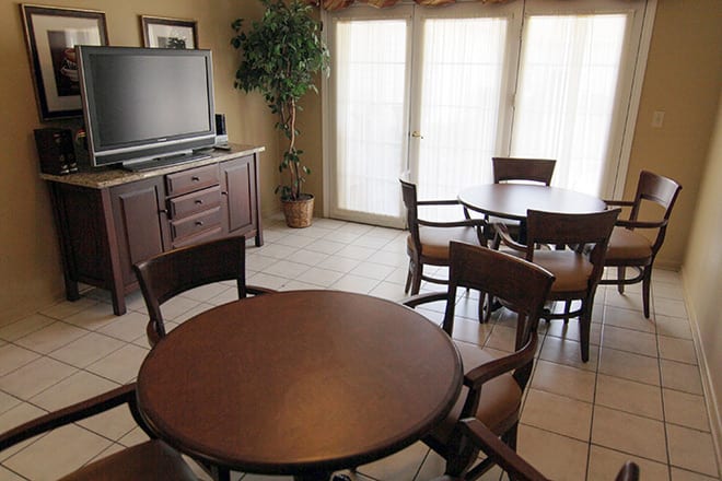 A cozy dining area with round tables, chairs, and a TV by large windows.
