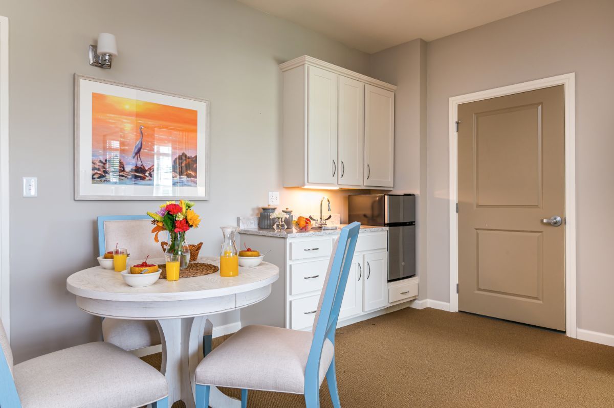 A cozy dining area with a round table and chairs, decorated in modern style with a kitchenette in the background.