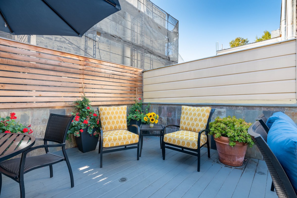 A cozy urban patio with stylish chairs and vibrant potted plants under a clear blue sky.