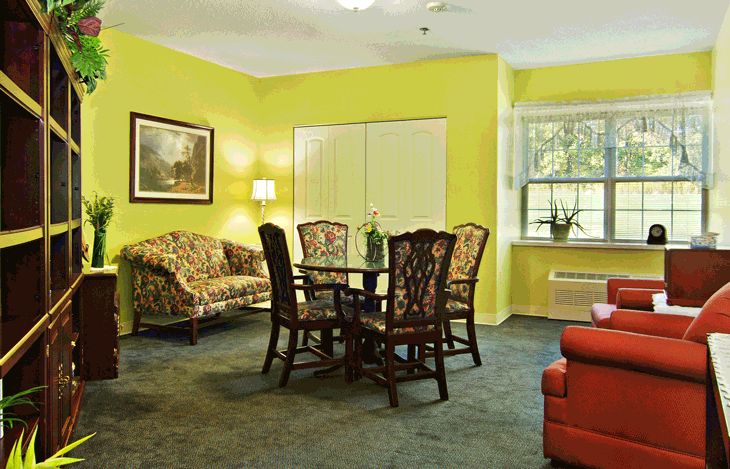 A cozy living room with a dining table, surrounded by chairs and a sofa, against bright yellow walls.