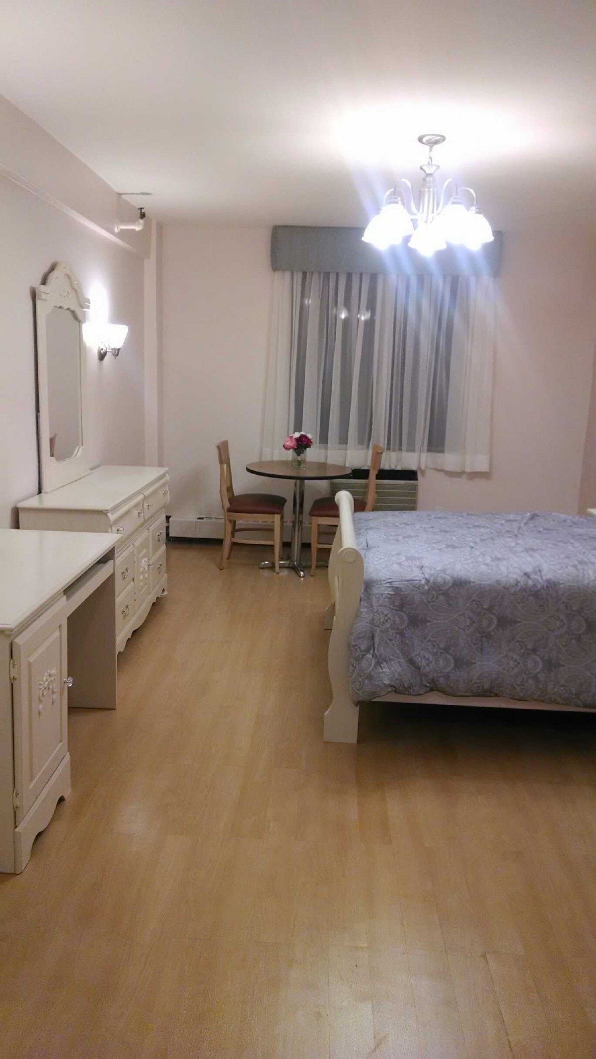 A cozy bedroom with a bed, dresser, and small dining table set.