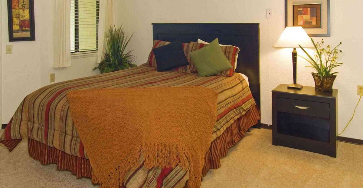 A cozy bedroom with a neatly made bed, accent pillows, and warm lighting.