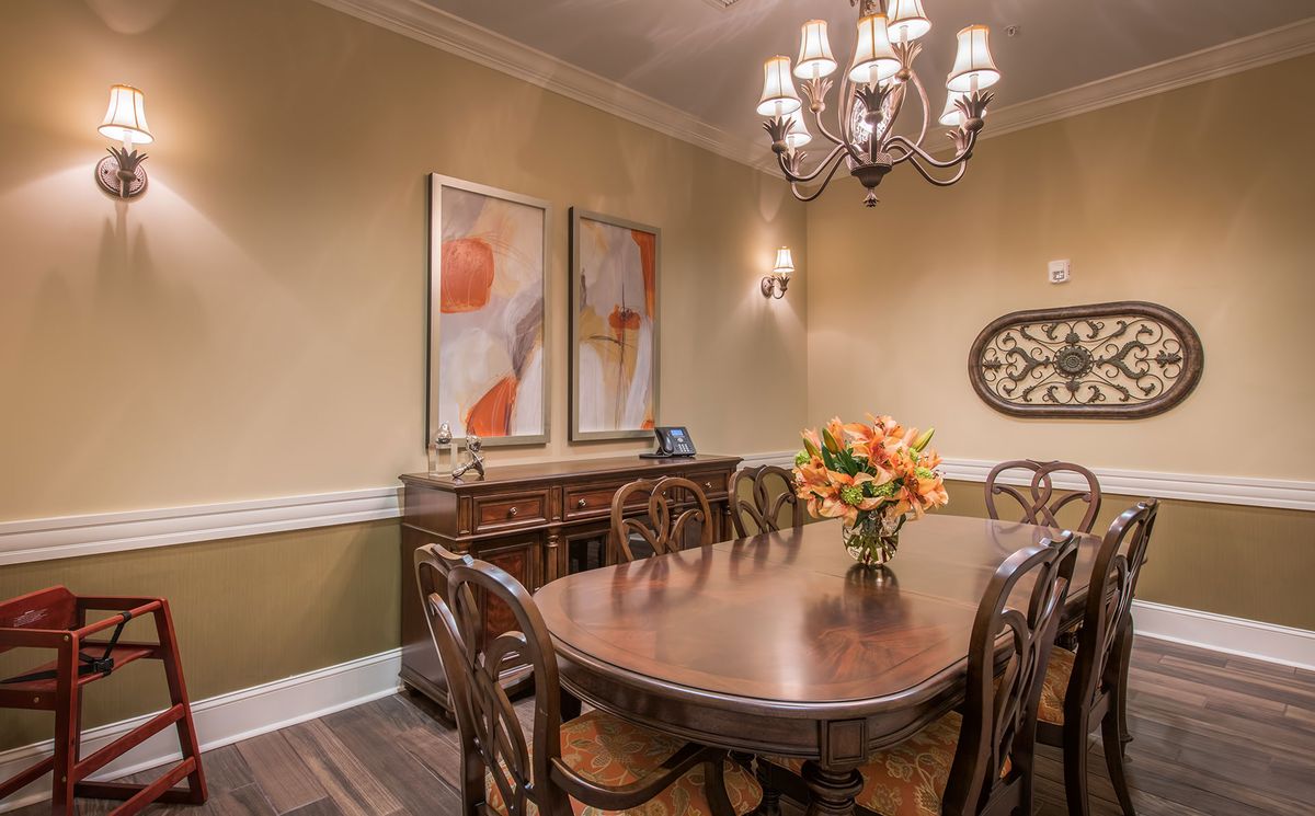 A cozy dining room featuring a wooden table and chairs, adorned with floral decor and elegant wall art under a classic chandelier.