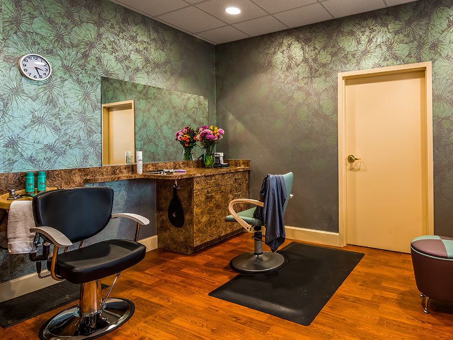 A cozy hair salon setup featuring chairs, a mirror, and decorative flowers.