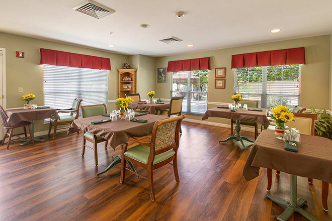 A cozy dining room with wooden floors, set with tables and chairs, and decorated with flowers.