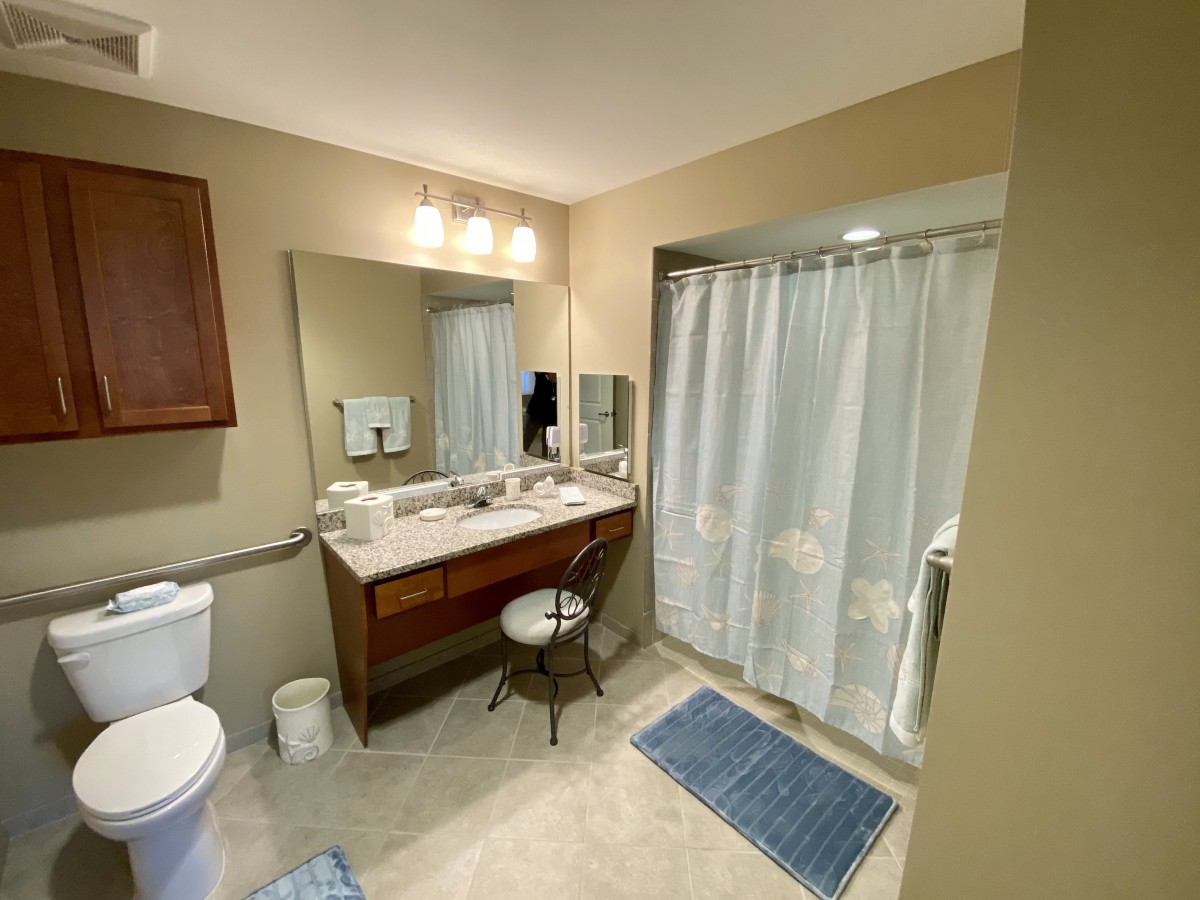 A well-lit bathroom featuring a large mirror, a sink with a countertop, and a shower with a curtain.