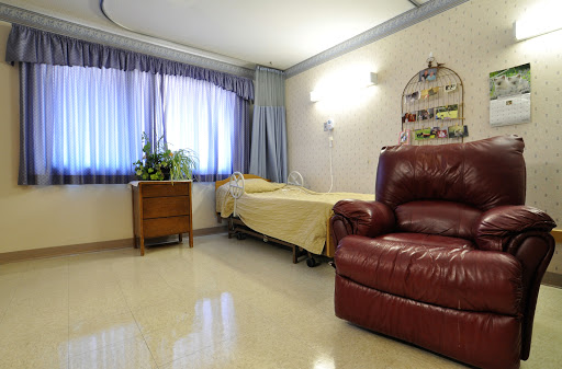 A cozy hospital room featuring a patient bed, a recliner chair, and natural light from the windows.