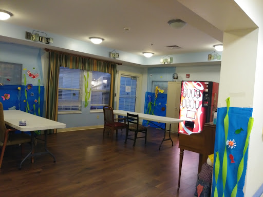 A spacious indoor room with tables, chairs, and a vending machine, featuring colorful decorative walls.