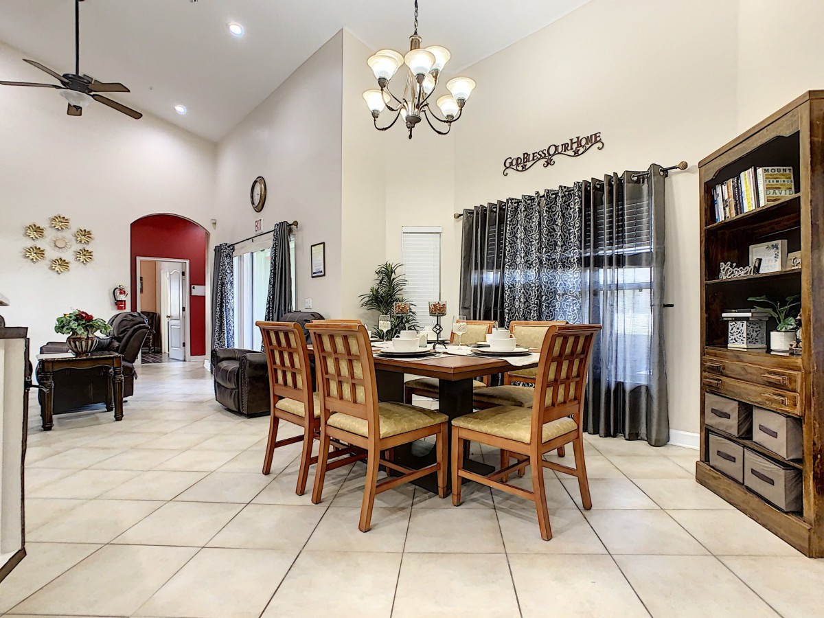 A spacious dining room with a round table, wooden chairs, and a chandelier overhead.