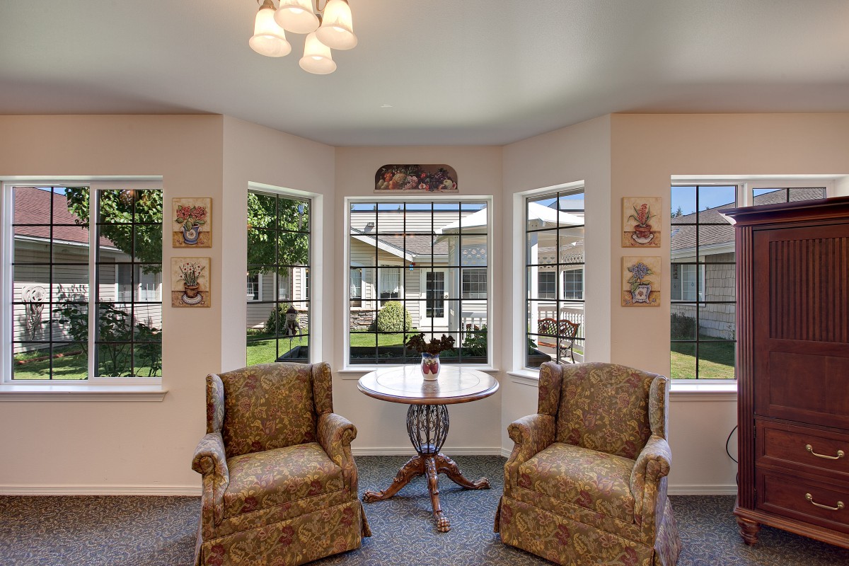 A cozy seating area with two armchairs and a round table by large windows, allowing natural light to fill the room.